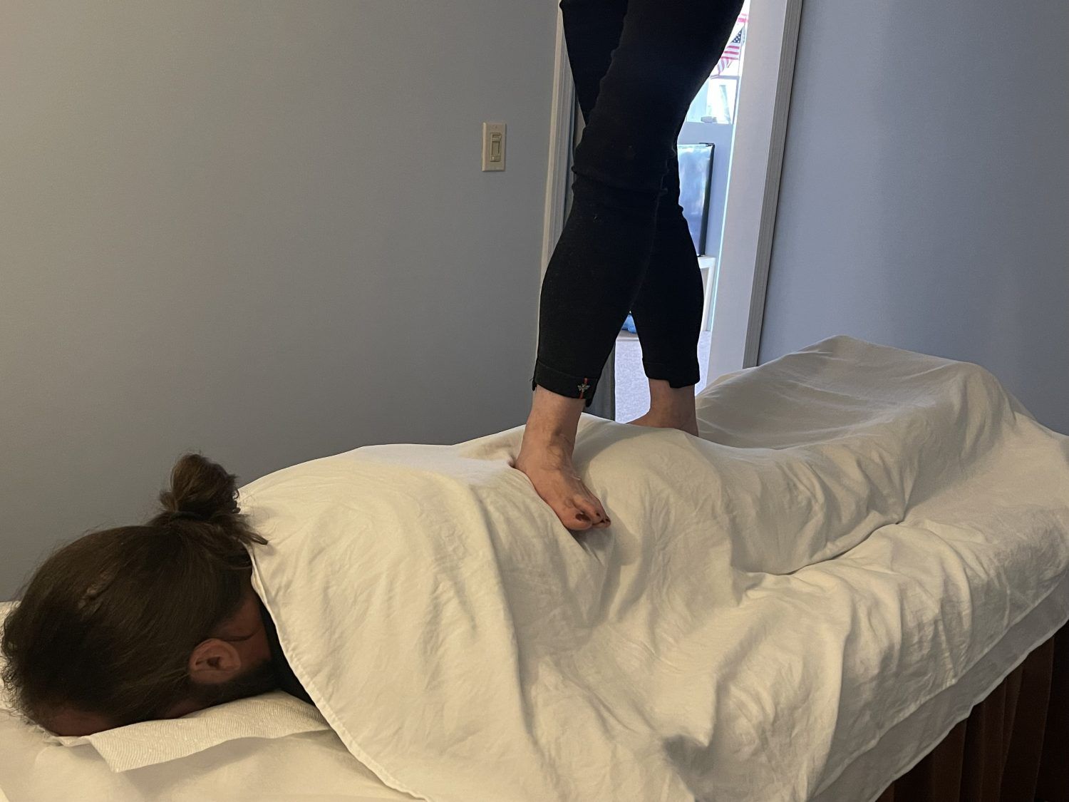 A client receiving an ashiatsu massage, where the therapist uses their feet to apply deep pressure for muscle tension relief.